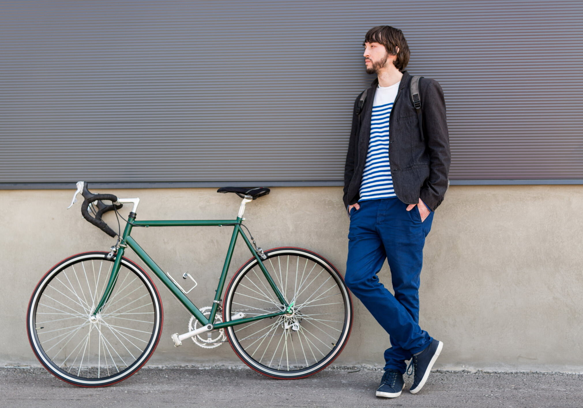 Portrait of a young attractive man wearing casual clothes posing with his bicycle against a wall